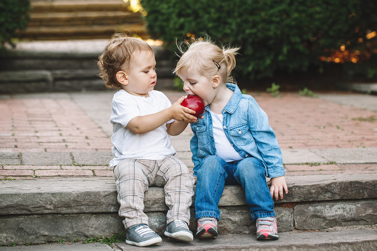 Two young children sharing an apple