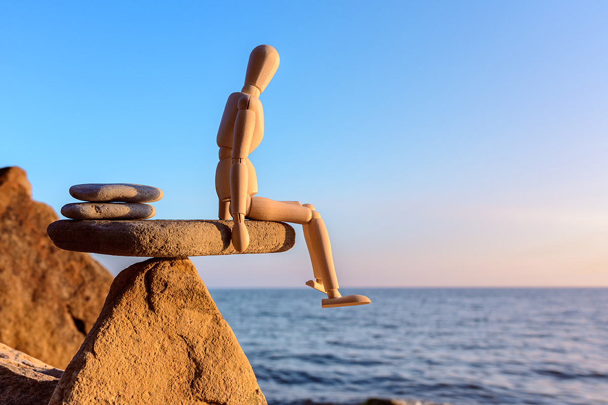 wooden mannequin sitting on rocks by sea