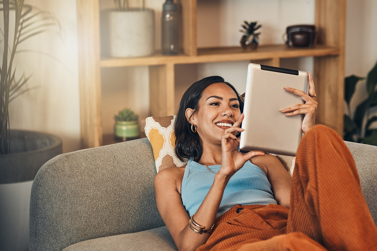 smiling woman on couch reading content on iPad